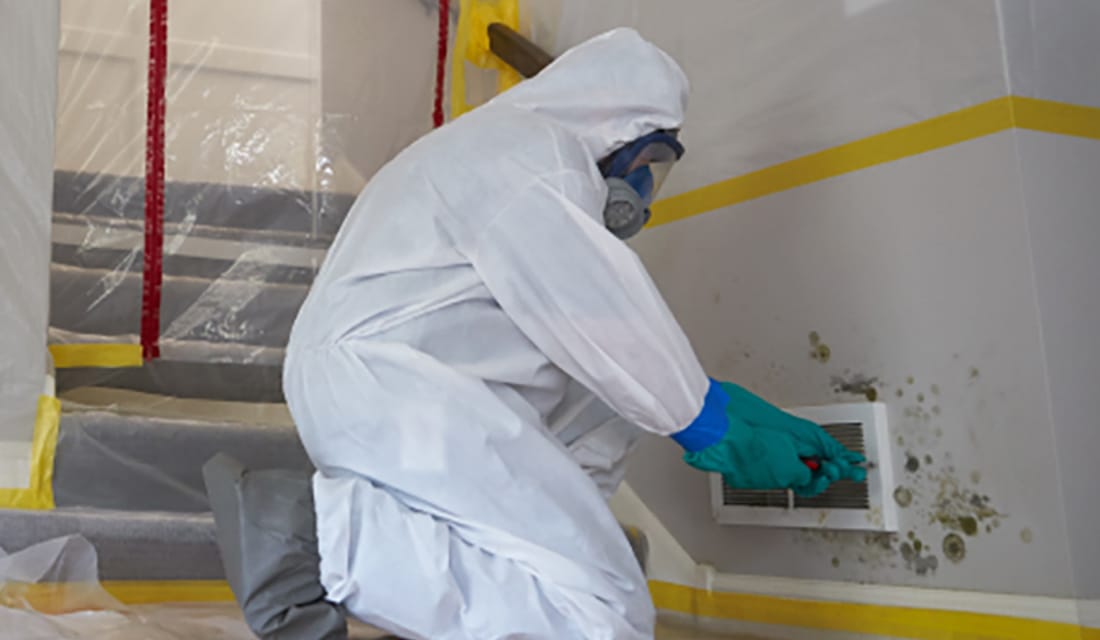 Technician in protective equipment working at an AC vent in a property